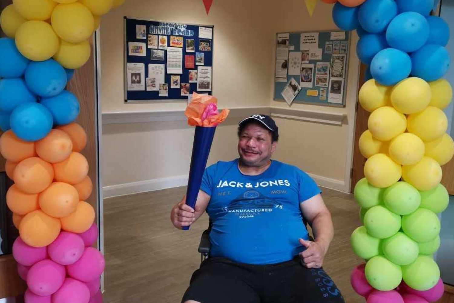 A male holding an Olympic torch under a balloon arch