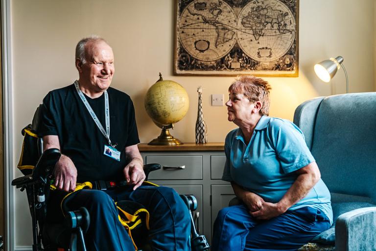 Picture of an older man using a wheelchair, talking to a female Support Worker