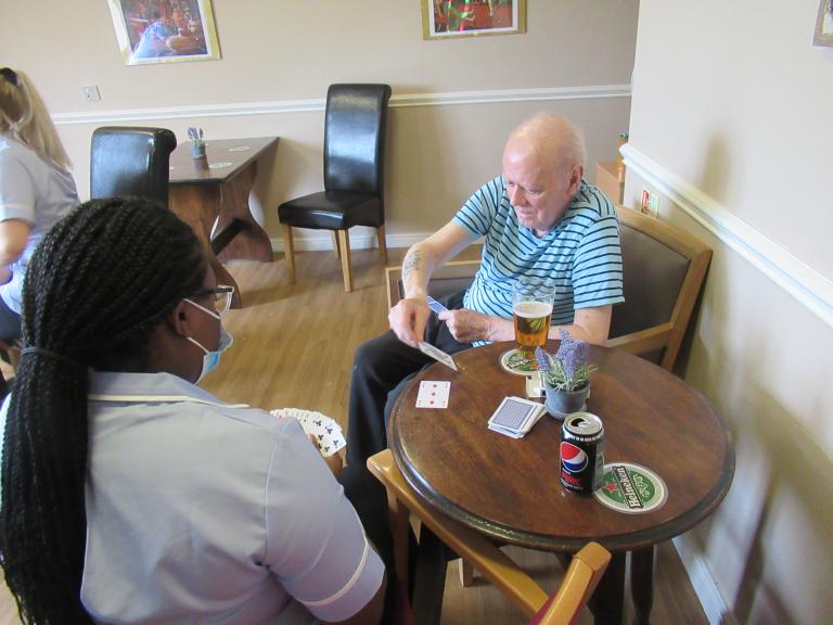 Photo of a male resident sat in the pub at our Scotia Heights care home playing cards with a Support Worker