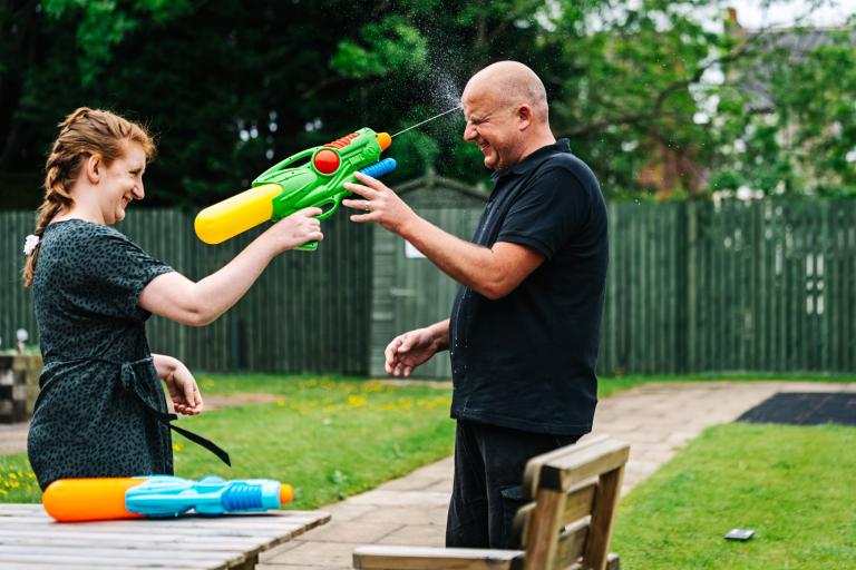 Young woman squirting water gun at male carer