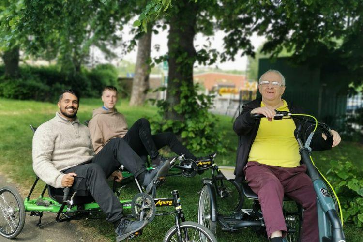 Male carer and male service users riding a bike in the park