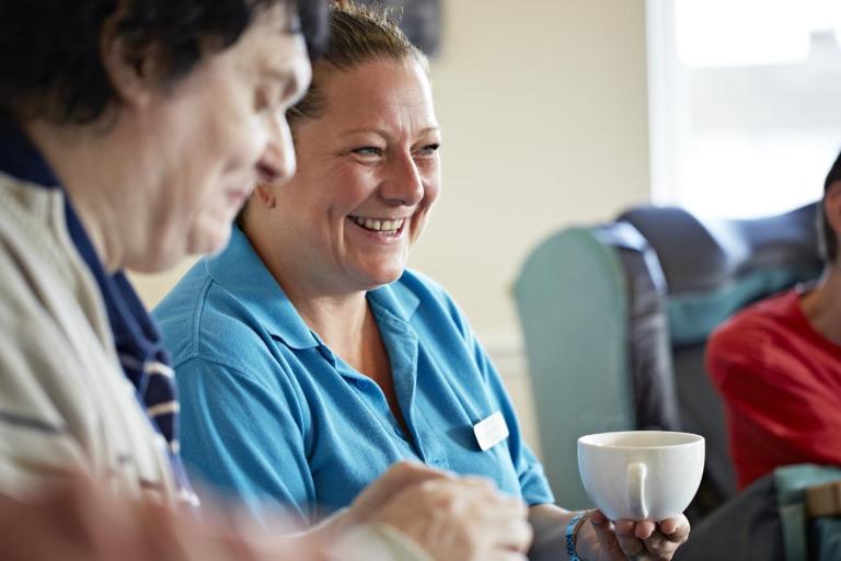 Care Assistant holding a cup of tea and smiling at camera